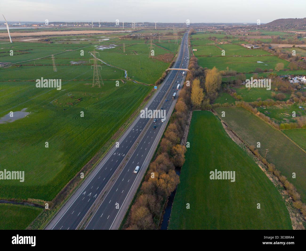 Une vue aérienne longue distance de l'autoroute M56 qui traverse la campagne du Cheshire près de Helsby, avec des pylônes électriques et des pâturages verts. Banque D'Images
