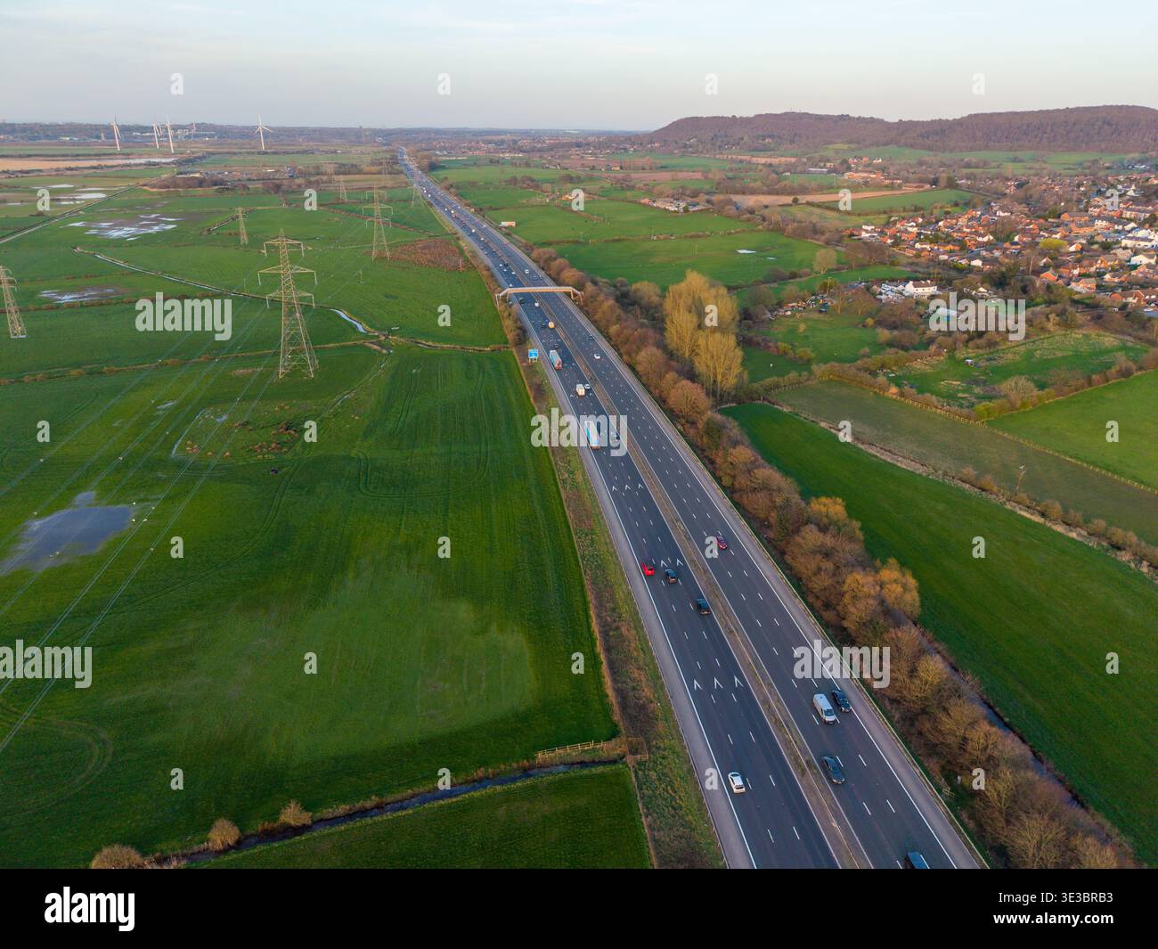 Une vue aérienne longue distance de l'autoroute M56 qui traverse la campagne du Cheshire près de Helsby, avec des pylônes électriques et des pâturages verts. Banque D'Images