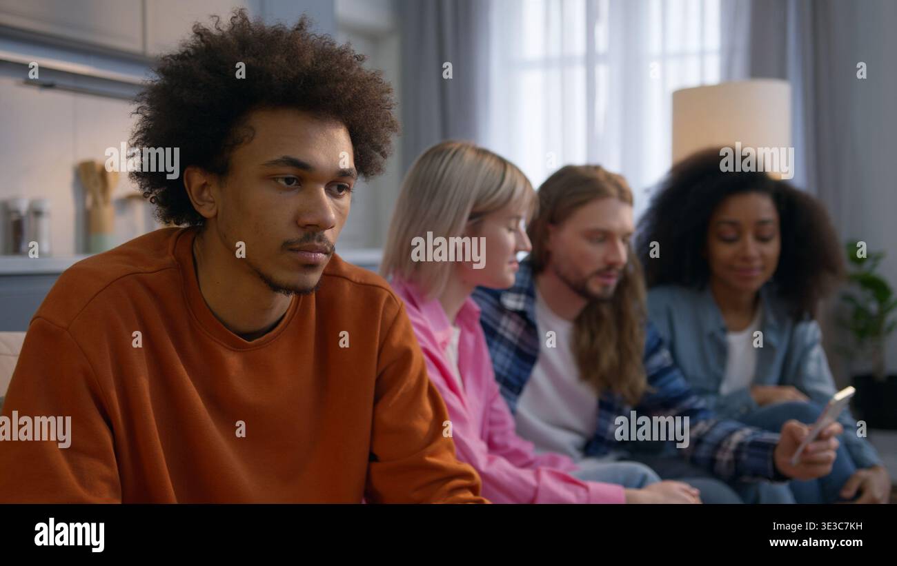 Homme afro-américain solitaire assis à la maison se sentant frustré mâle stressé isolé ignorant les amis caucasiens multiethniques femmes hommes discutant Banque D'Images