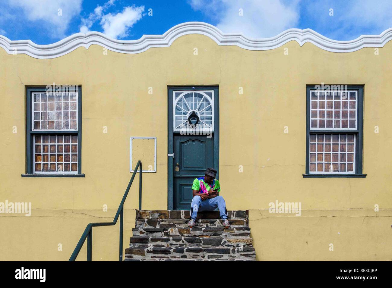 Un moment de calme sur des marches ensoleillées sous une façade jaune éclatante, où la couleur, la culture et le calme se rencontrent Banque D'Images