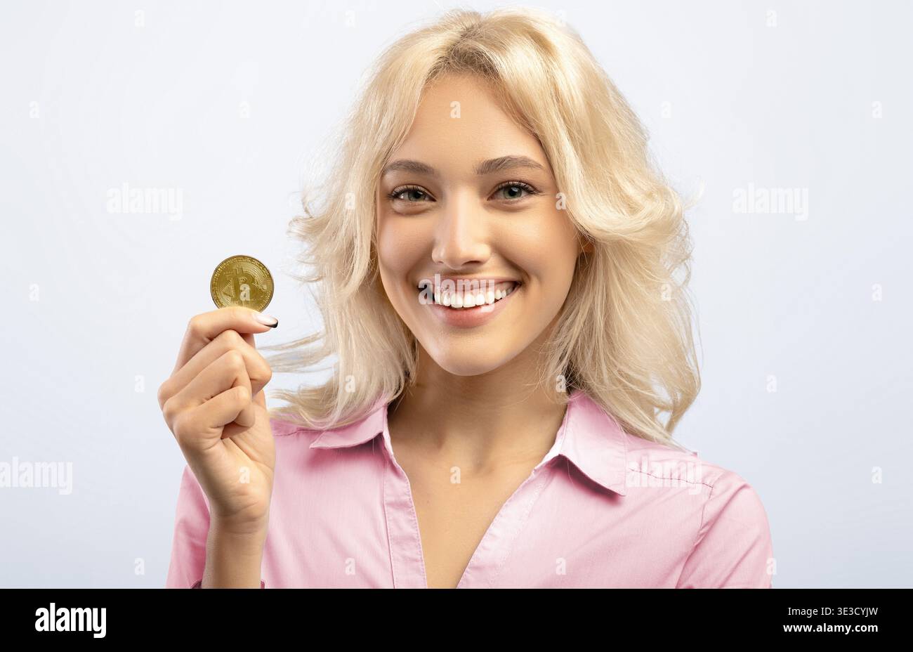 Femme tenant une pièce d'or et souriant lors d'un tournage en studio dans la lumière naturelle Banque D'Images