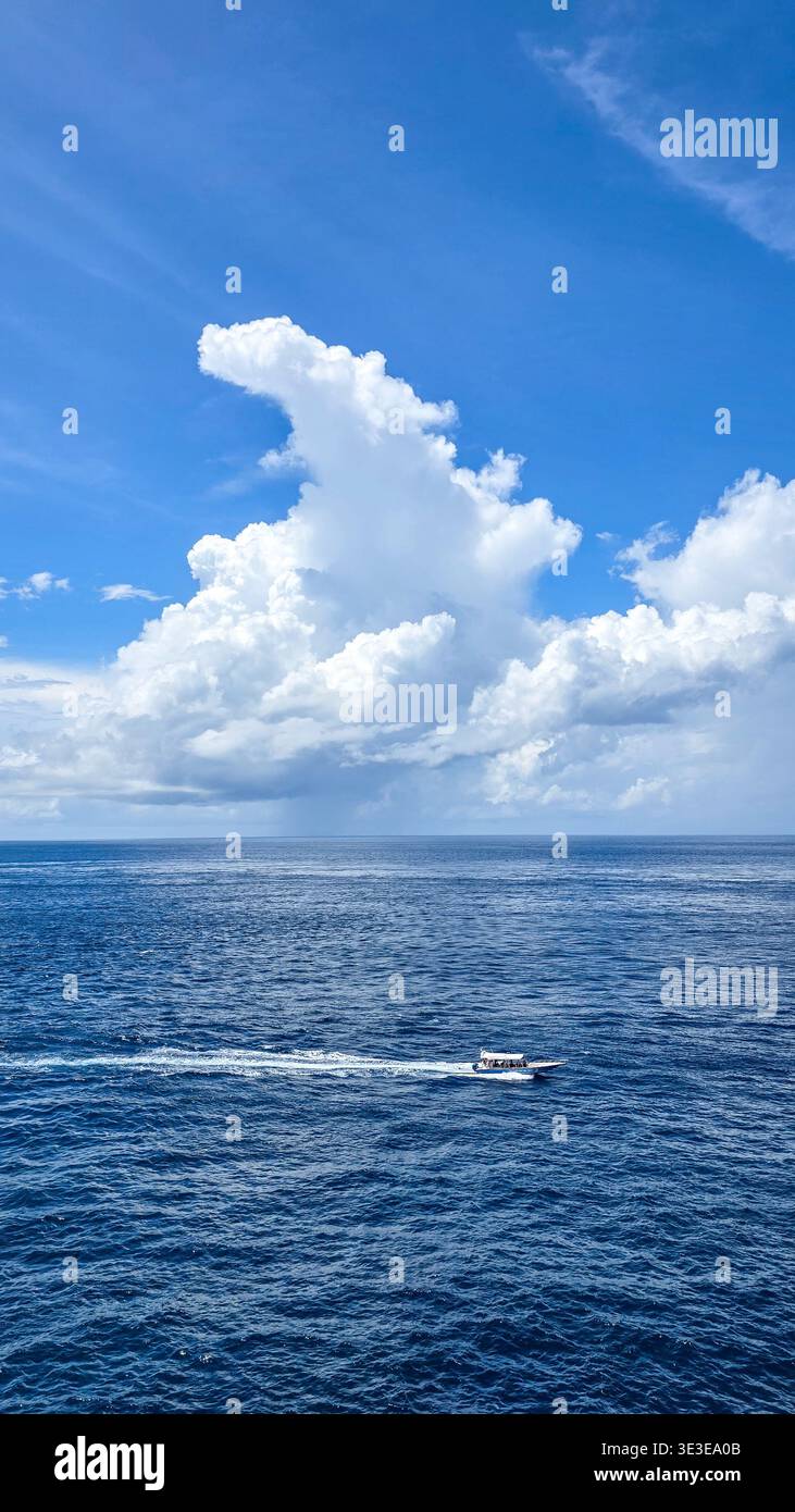Petit bateau à moteur naviguant à travers l'océan bleu profond sous un vaste ciel rempli d'imposants nuages de cumulus blancs, capturant une scène maritime paisible - Image de stock capturée avec un smartphone