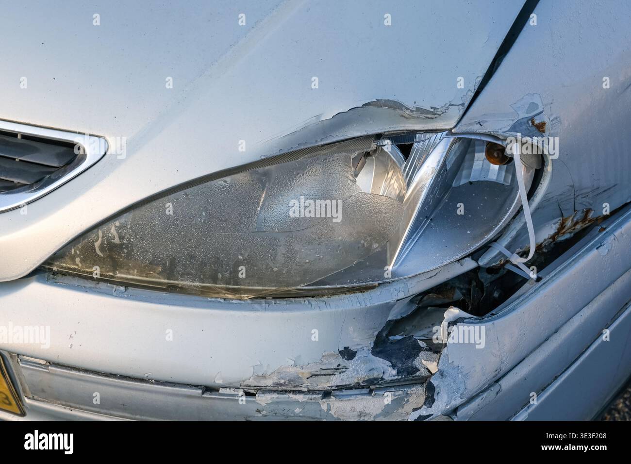Phare de voiture endommagé et pare-chocs avant cassé après un accident de la route gros plan avec plastique fissuré et carrosserie blanche rayée Banque D'Images