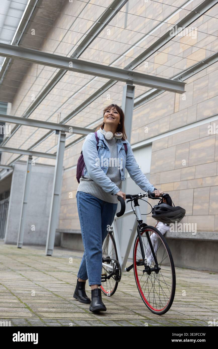 Vélo de route de randonnée féminin sous la verrière sur la passerelle carrelée, regardant vers le haut, souriant, casque suspendu Banque D'Images