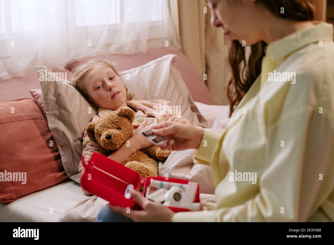 Enfant couché dans le lit tenant un ours jouet pendant que mère prépare des médicaments Banque D'Images