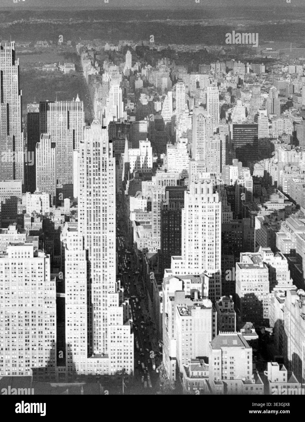 Cette photographie aérienne en noir et blanc saisissante capture un paysage urbain dense de gratte-ciel de New York, probablement des années 1940 Les longues ombres projetées par les grands bâtiments sur les avenues en contrebas soulignent la grandeur architecturale de la ville et l'activité animée au niveau de la rue. Photographiée par Angelo Rizzuto, cette image offre un aperçu historique de l'emblématique skyline de Manhattan. Banque D'Images