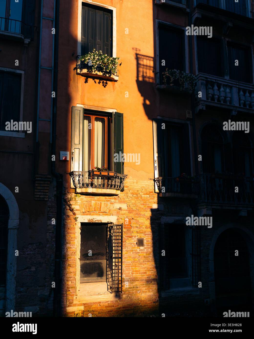 Vue des bâtiments rustiques orange avec des ombres contrastées et des façades ensoleillées créant une atmosphère chaleureuse et accueillante, Venise, Vénétie, Italie. Banque D'Images