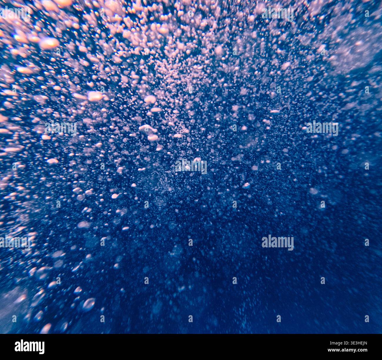 Bulles s'élevant dans l'eau bleu profond avec filtrage de la lumière à travers, créant un effet sous-marin texturé. Banque D'Images