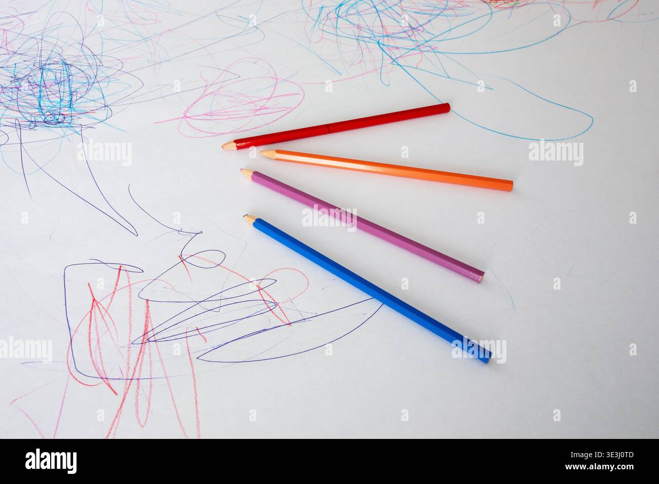 Crayons en bois colorés non aiguisés reposant sur une surface de papier blanc recouverte de gribouilles et de dessins d'enfant Banque D'Images