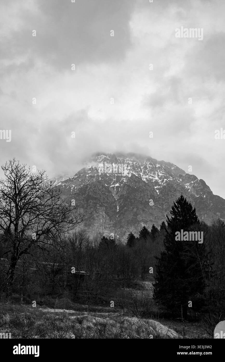Vue à travers une ruelle étroite entre les bâtiments menant à la structure rustique et paysage de montagne en arrière-plan dans le cadre du village du nord de l'Italie. Banque D'Images