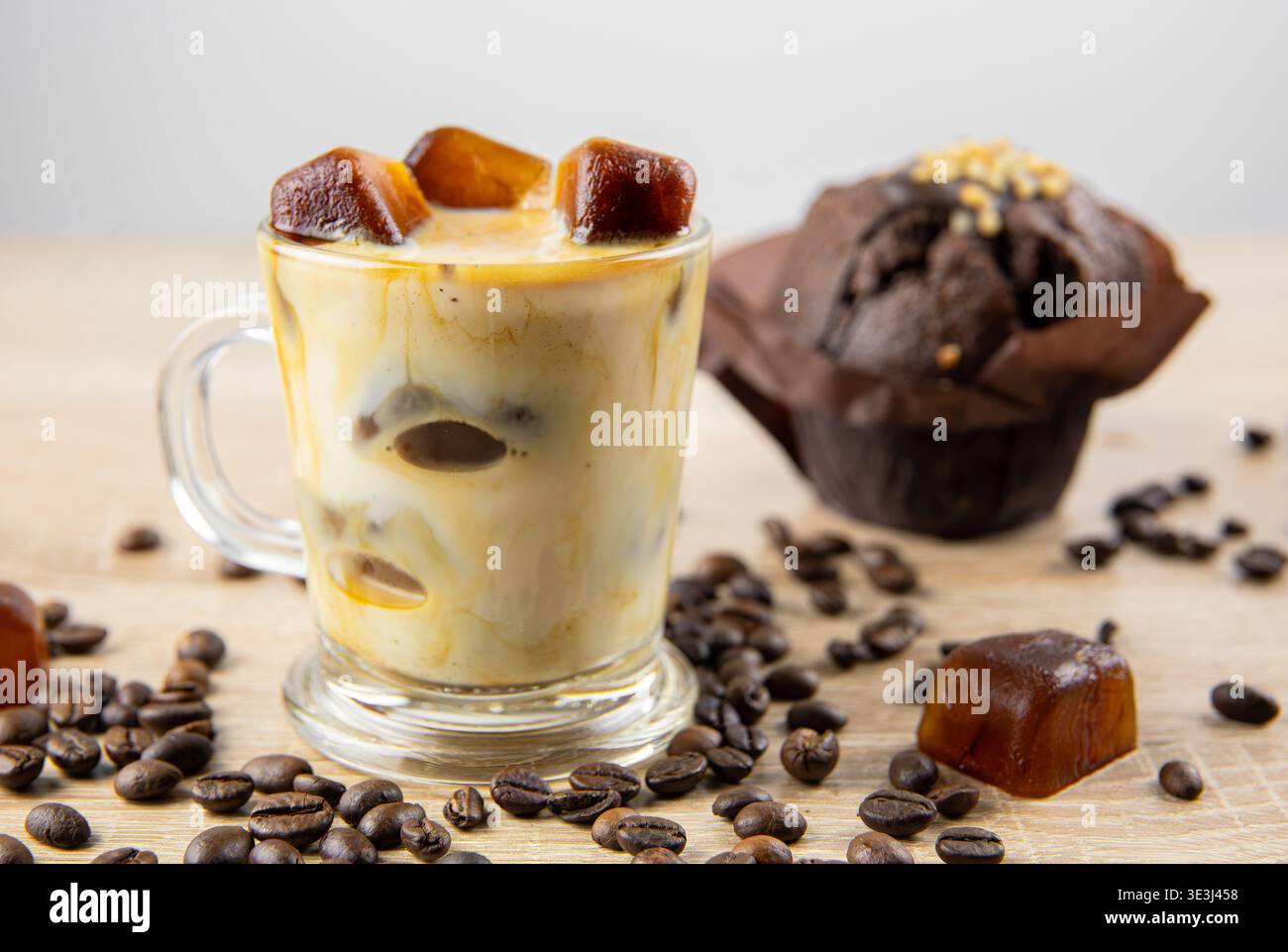 Vue de côté de boisson au café glacé avec du lait, glaçons au café dispersés sur la table, décorés avec des grains de café. Prise de vue en studio. Concept de glaçons au café f Banque D'Images