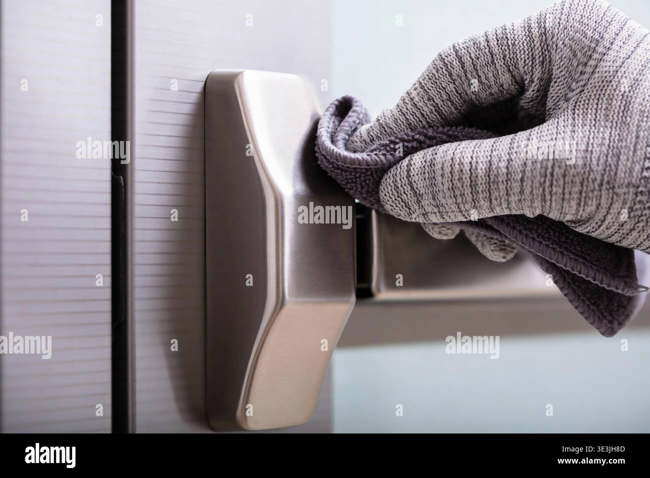 Une personne portant un gant de protection nettoie méticuleusement une poignée de porte moderne avec un chiffon doux, mettant l'accent sur l'hygiène et les soins Banque D'Images