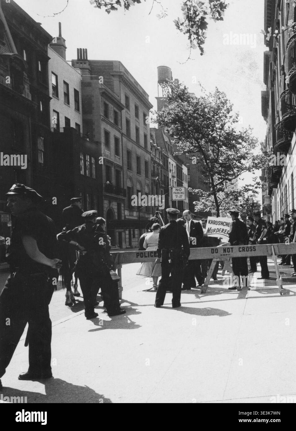 Cette photographie de rue vintage, probablement capturée par Angelo Rizzuto dans les années 1960, représente une barrière de police gérant une manifestation ou un rassemblement public à New York. De nombreux policiers se tiennent à côté de barricades en bois marquées « POLICE DEPT ». Et "NE PAS TRAVERSER", tandis qu'un panneau disant "MEURTRIER DE KHROUCHTCHEV" est visible en arrière-plan, offrant un aperçu du climat politique de l'époque. Banque D'Images