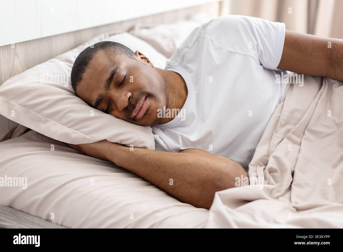 Beau jeune homme noir dormant paisiblement sur le lit sous une couverture Banque D'Images