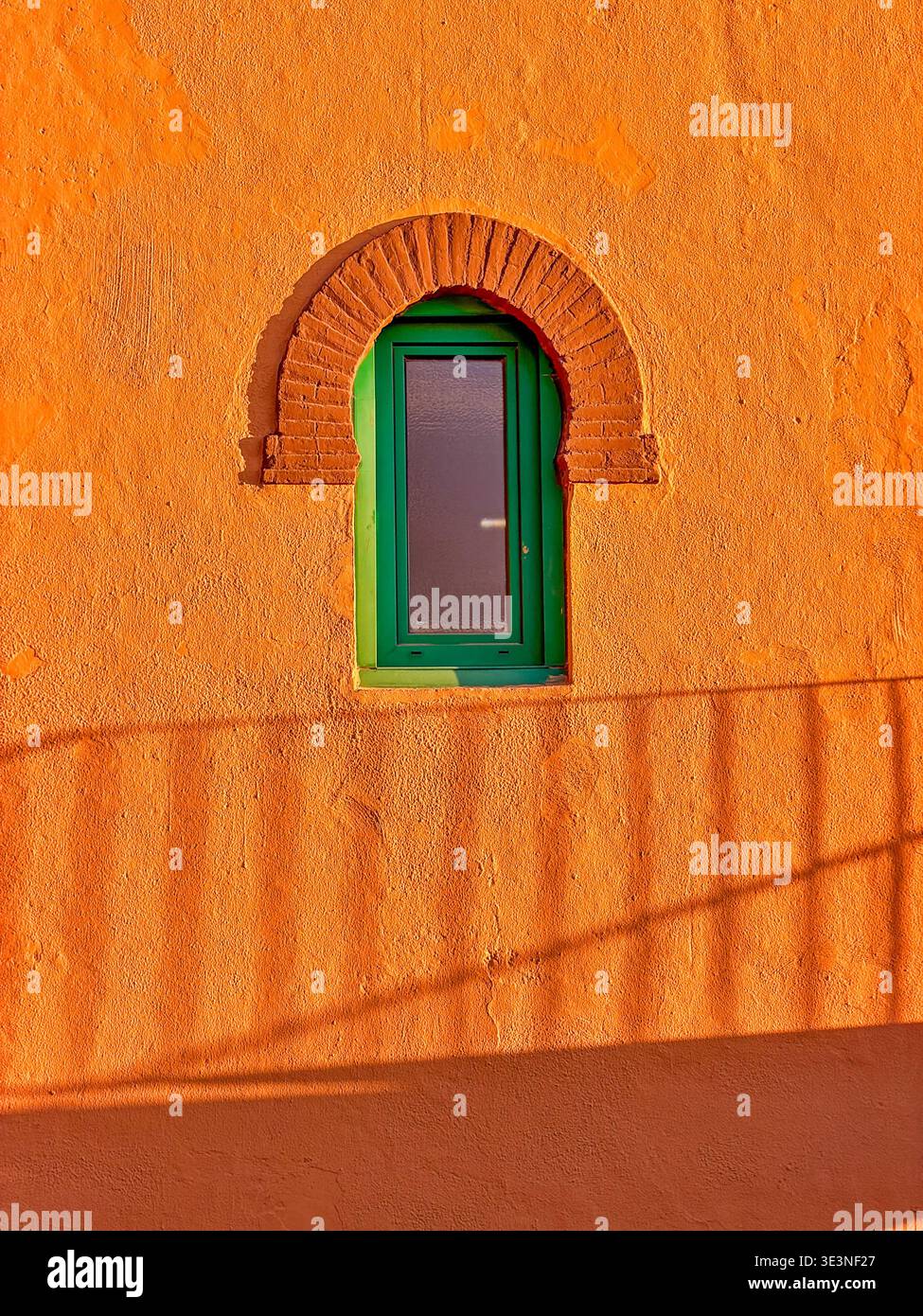 Un mur orange profond fournit un fond pour une fenêtre verte et l'ombre d'une main courante sur un bâtiment anonyme à Grenade. Espagne. Banque D'Images