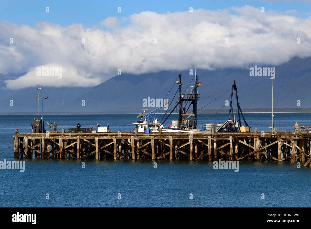 Les gens sur le quai avec un bateau de pêche à Jackson Bay, côte ouest, île du Sud, Nouvelle-Zélande Banque D'Images
