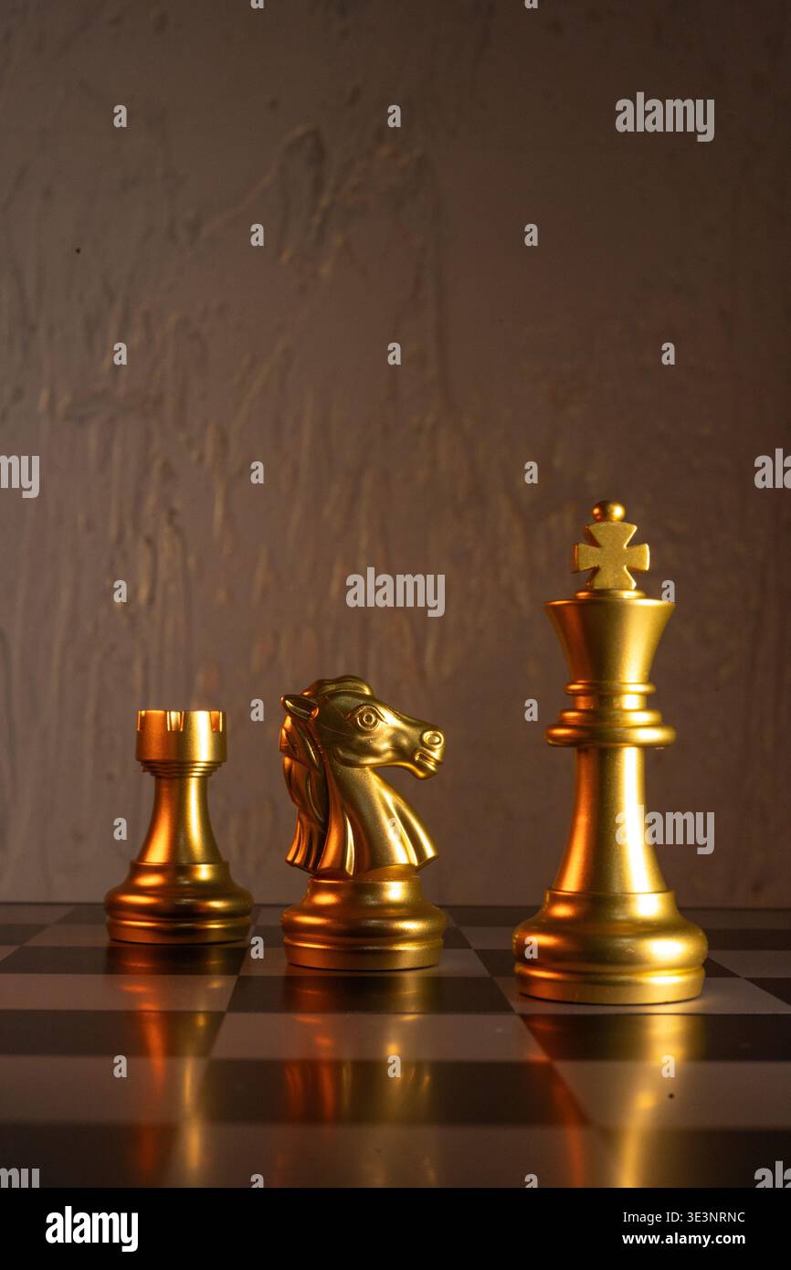 Composition de trois pièces d'échecs dorées - tour, chevalier et roi dans des positions debout stables sur un tableau noir et blanc. Banque D'Images
