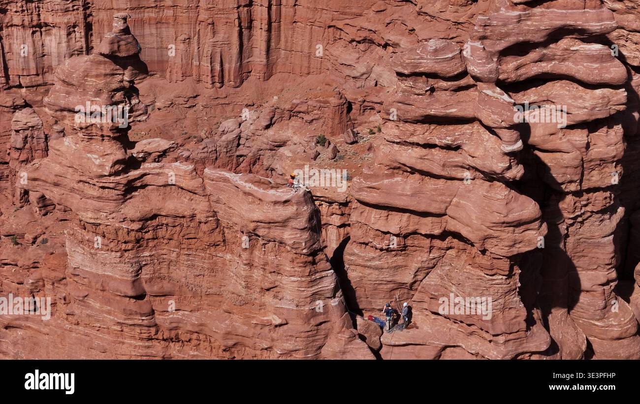Vue aérienne de grimpeurs perchés sur une formation de grès, le rocher rouge contrastant avec le vaste ciel bleu, Moab, Utah, États-Unis. Banque D'Images