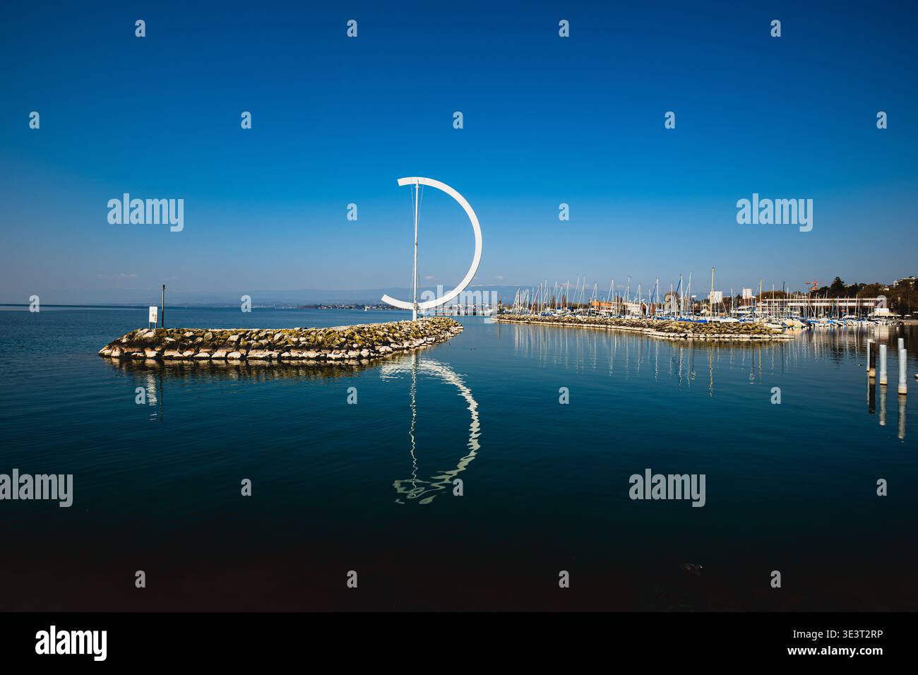 Lausanne, Suisse, 21 mars 2026. Sculpture moderne en croissant blanc Eole sur un lac bleu calme reflétant dans la surface de l'eau calme Banque D'Images