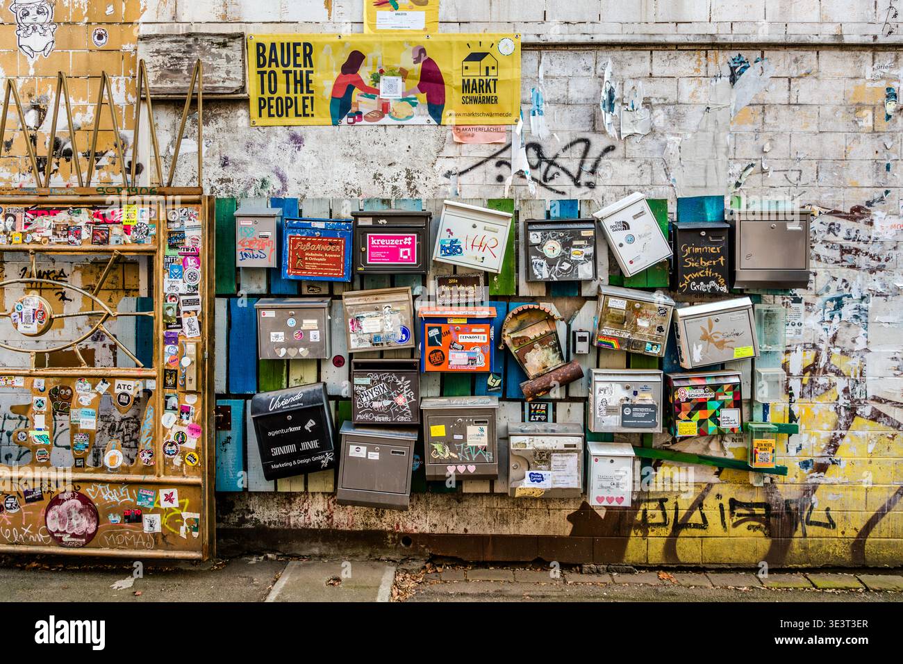 Un mur de bâtiment densément couvert avec des dizaines de boîtes aux lettres colorées de différents motifs, autocollants et graffitis ; au-dessus, une affiche portant les mots « Bauer to the People » et une pancarte pointant vers le marché Connewitz. Leipzig, Saxe, Allemagne Banque D'Images