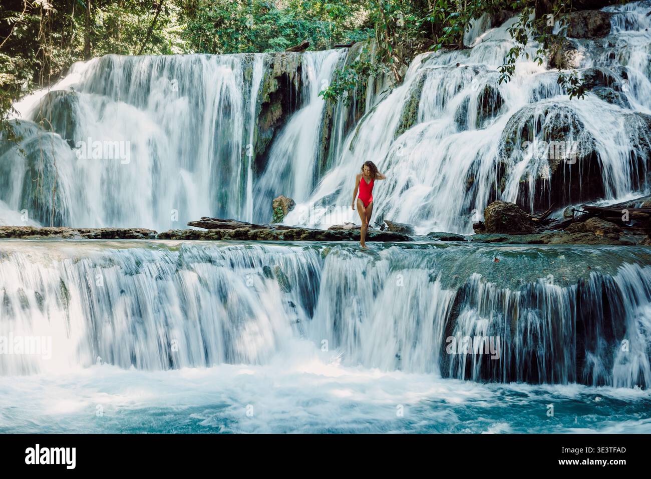 Femme en maillot de bain rouge marchant à travers la cascade tropicale de cascade dans le paysage luxuriant de la jungle Banque D'Images