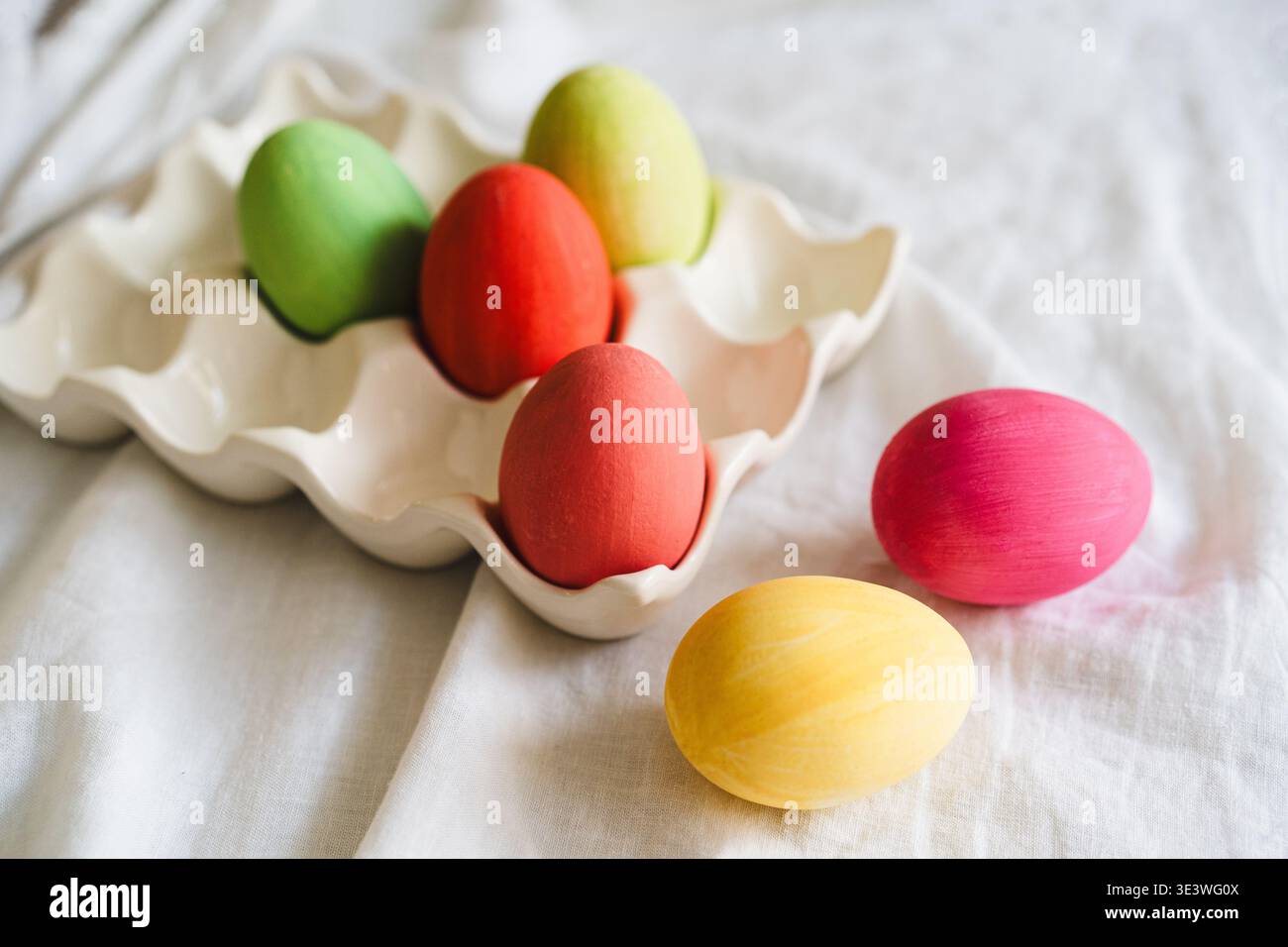 Oeufs de Pâques multicolores affichés dans un élégant plateau à oeufs sur un fond de tissu blanc doux. Cette collection vibrante d'œufs incarne le spir festif Banque D'Images