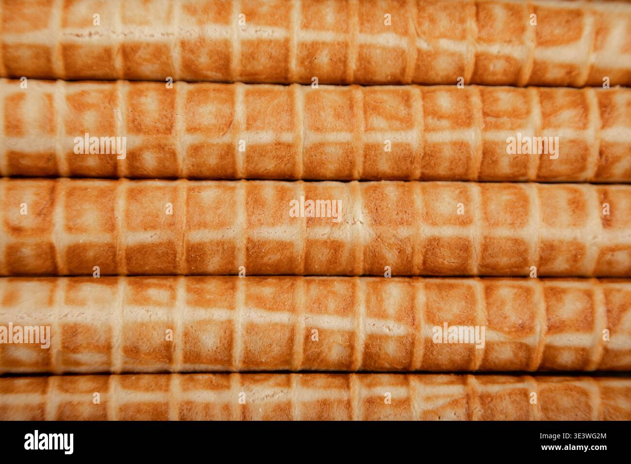 Gros plan de tubes gaufrés cuits disposés en pile nette. Chaque tube présente une texture croustillante, brun doré, soulignant le délicieux treillis Banque D'Images