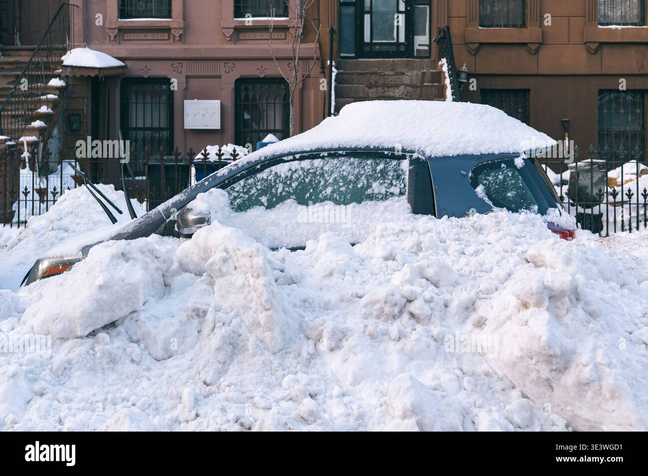 Une voiture enneigée enterrée sous une forte neige dans une rue urbaine, montrant les conséquences d'une tempête hivernale. La scène reflète les défis hivernaux dans un b. Banque D'Images