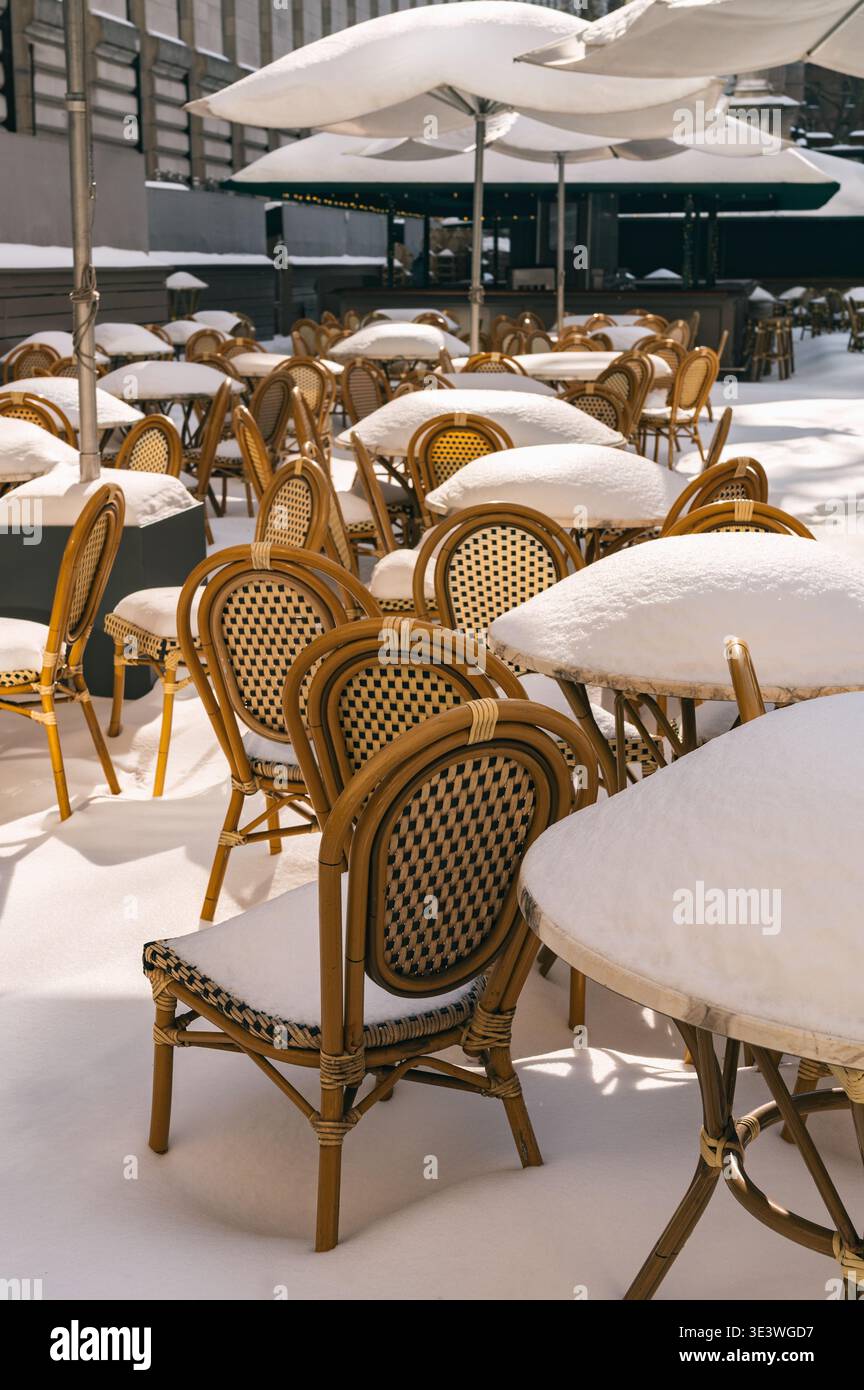 Une terrasse de café en plein air est recouverte de neige fraîche, laissant les tables et les chaises intactes dans une scène hivernale urbaine sereine. Les suites tranquilles d'un lourd Banque D'Images