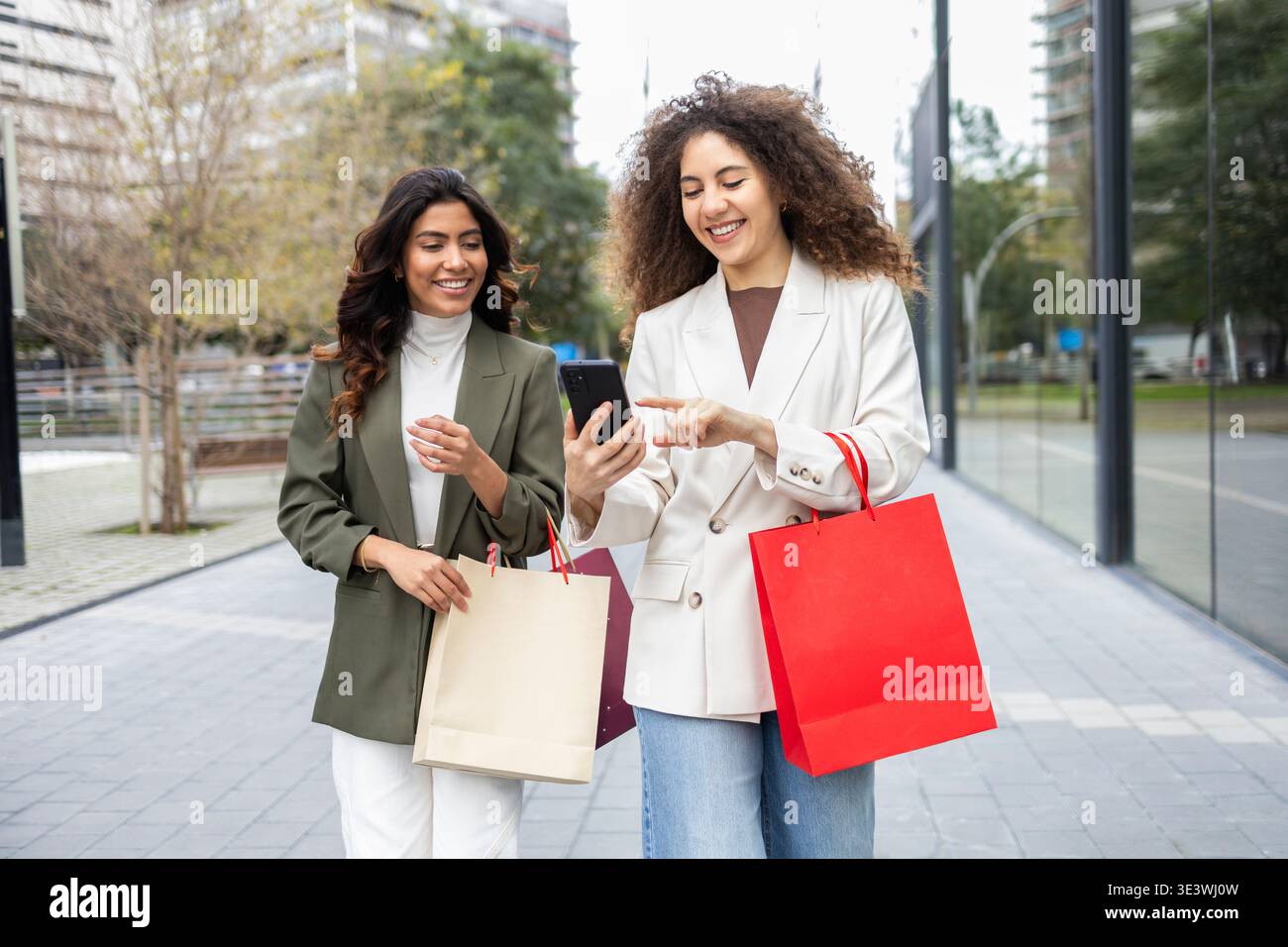 Deux femmes marchant dans une rue de la ville joyeusement bavardant et tenant des sacs à provisions. Ils semblent heureux et confiants, incarnant l'amitié, les affaires, et un v Banque D'Images