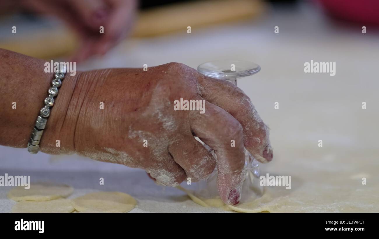 Les mains pressent un petit verre sur la pâte roulée pour couper des morceaux ronds sur un comptoir de cuisine. La vidéo montre la préparation de pâtisserie maison, utile pour Banque D'Images