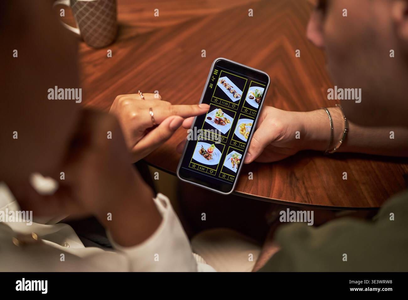 Femme jeune adulte caucasienne et homme jeune adulte caucasien assis à la table parcourant l'application de livraison de nourriture sur smartphone, femme à l'aide du doigt pour sélectionner le repas à partir du menu numérique, les mains rapprochées Banque D'Images