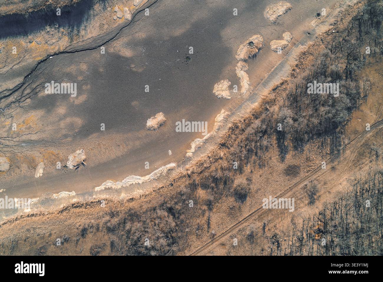 Vue aérienne désolée d'un lit de ruisseau sec traversant un paysage aride. La terre desséchée et le cours d'eau vide symbolisent le besoin urgent de conservation de l'environnement et d'action climatique mondiale face à la hausse des températures. Banque D'Images