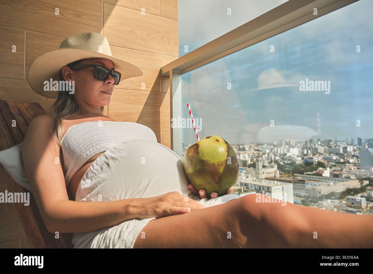 Femme enceinte profitant d'une boisson tropicale et vue sur la ville depuis le balcon de l'hôtel Banque D'Images