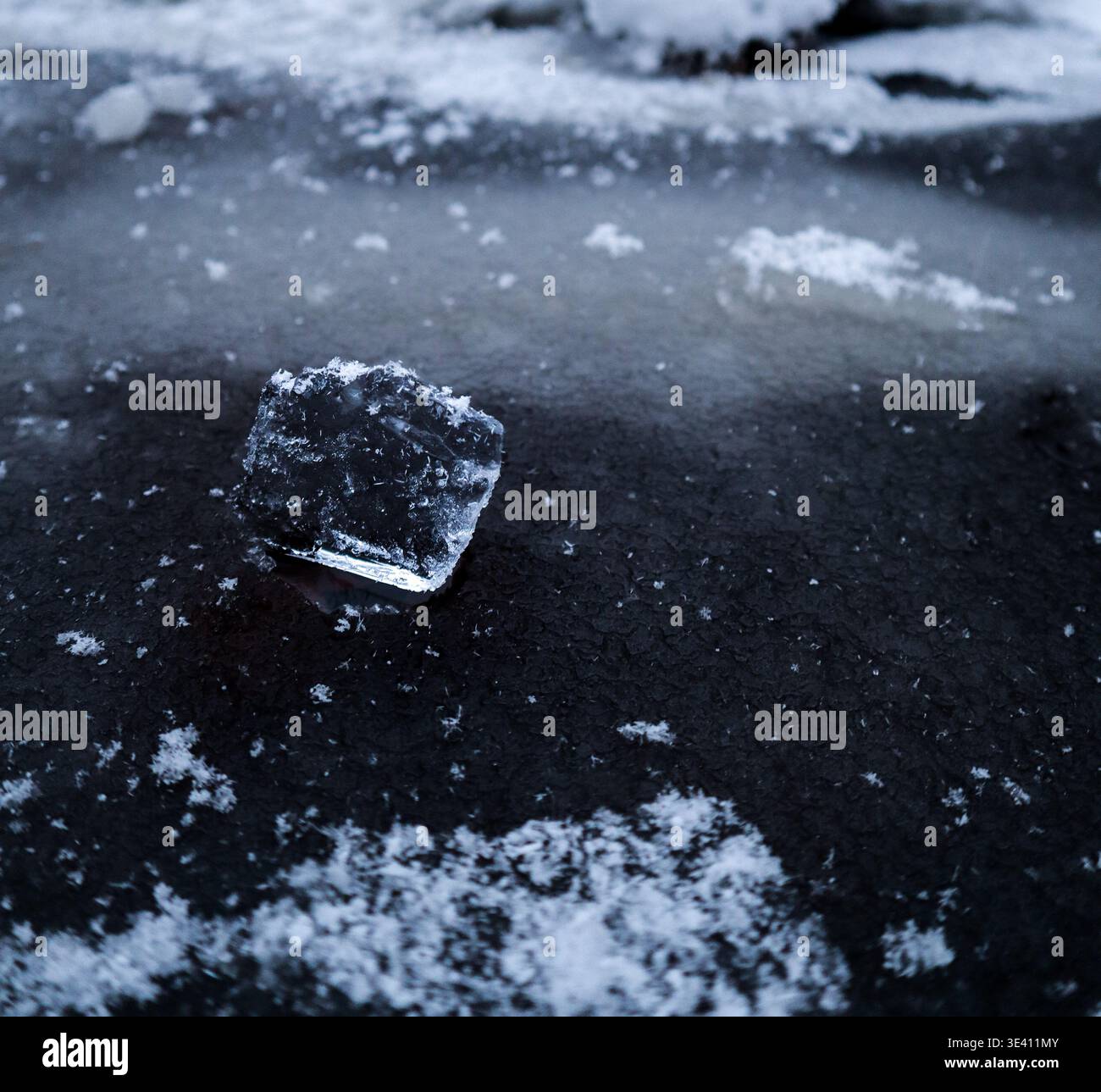 Petit morceau de glace sur une surface gelée avec flocons de neige dispersés, détails froids de l'hiver et texture de la nature Banque D'Images