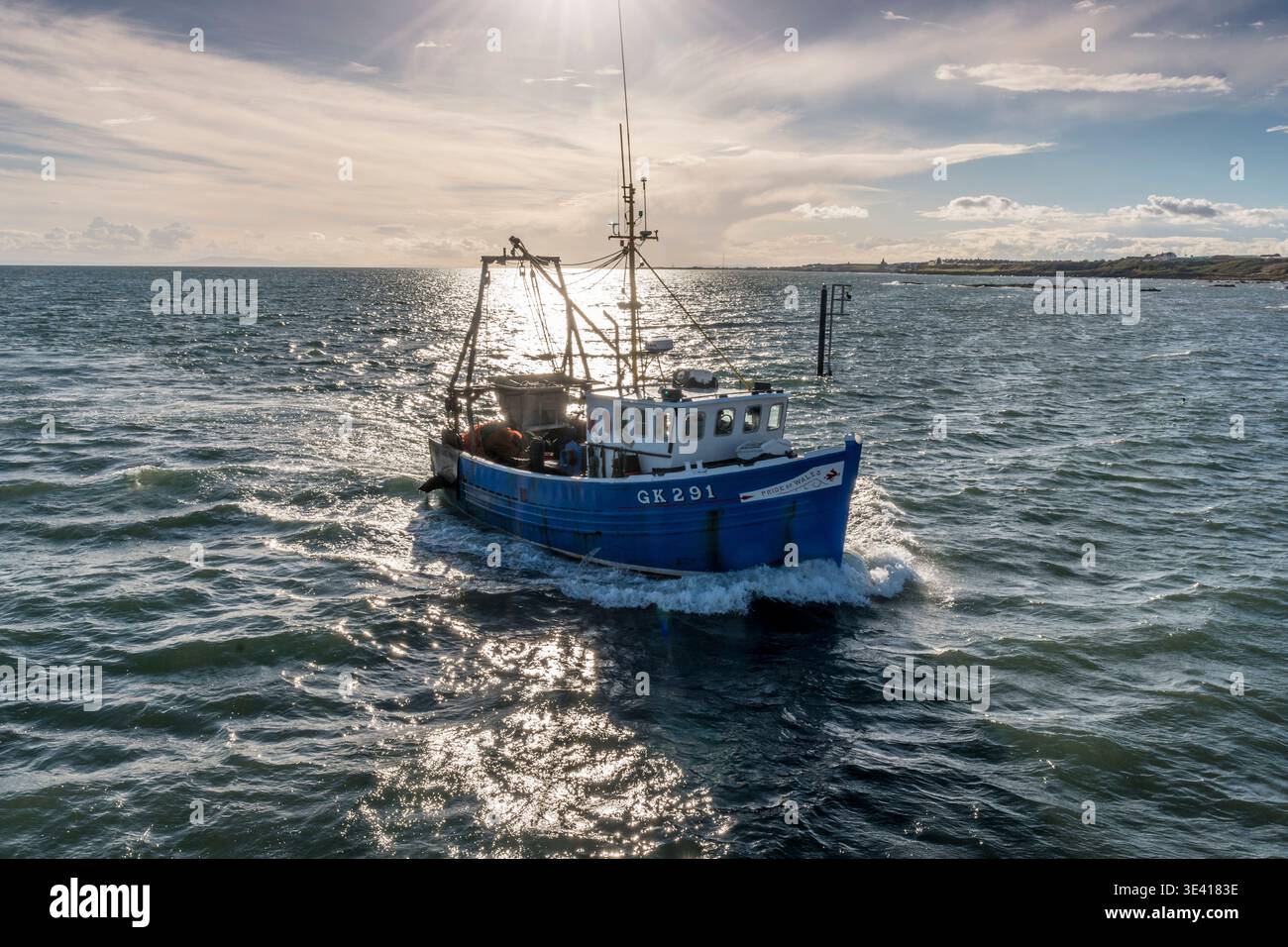 Un chalutier de pêche bleu rentre à la maison à travers des mers agitées ensoleillées vers le port de Pittenweem, montrant l'équipement de l'équipage, l'eau réfléchissante et la ligne d'horizon côtière qui e Banque D'Images
