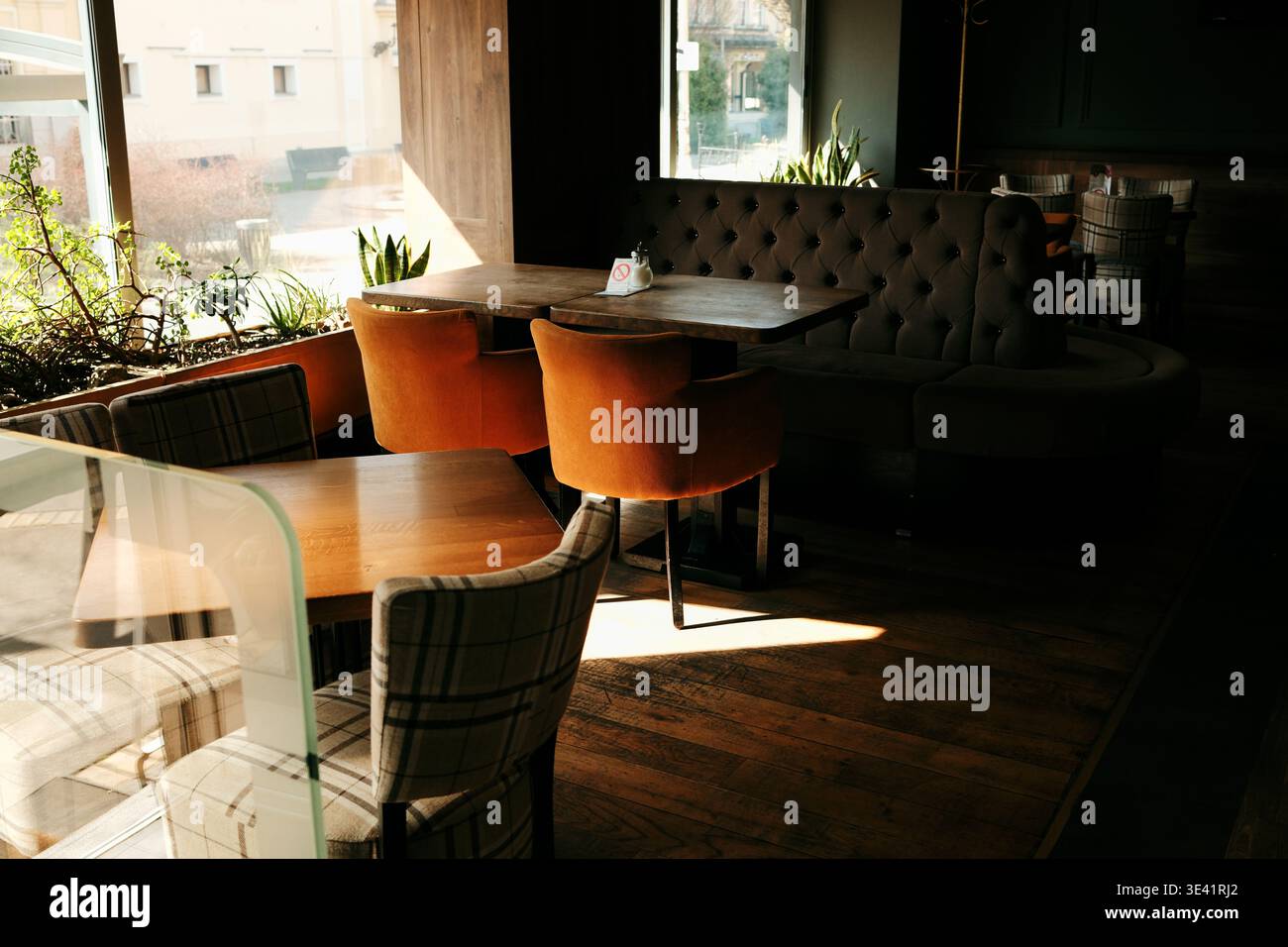 Intérieur de café moderne avec tables en bois, chaises moelleuses et lumière chaude du soleil à travers la fenêtre. Concept de confort, d'hospitalité et d'espace salle à manger élégant. Banque D'Images