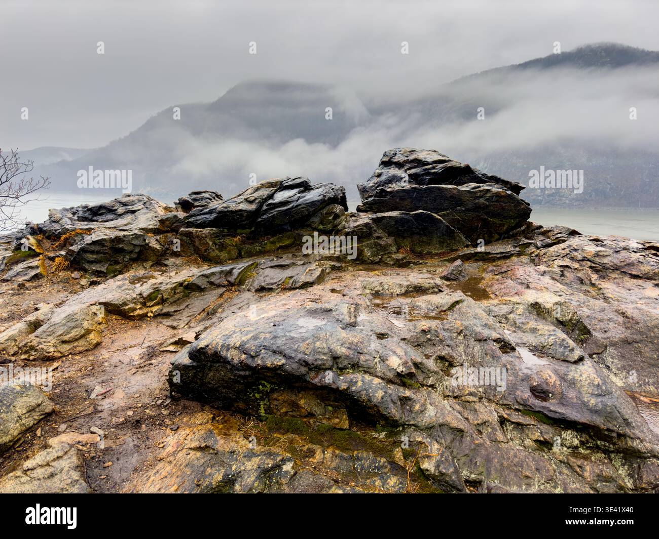 Affleurement rocheux humide au-dessus de la rivière Hudson dans les Hudson Highlands, avec du brouillard et des nuages bas à travers les montagnes de l'État de New York. Banque D'Images