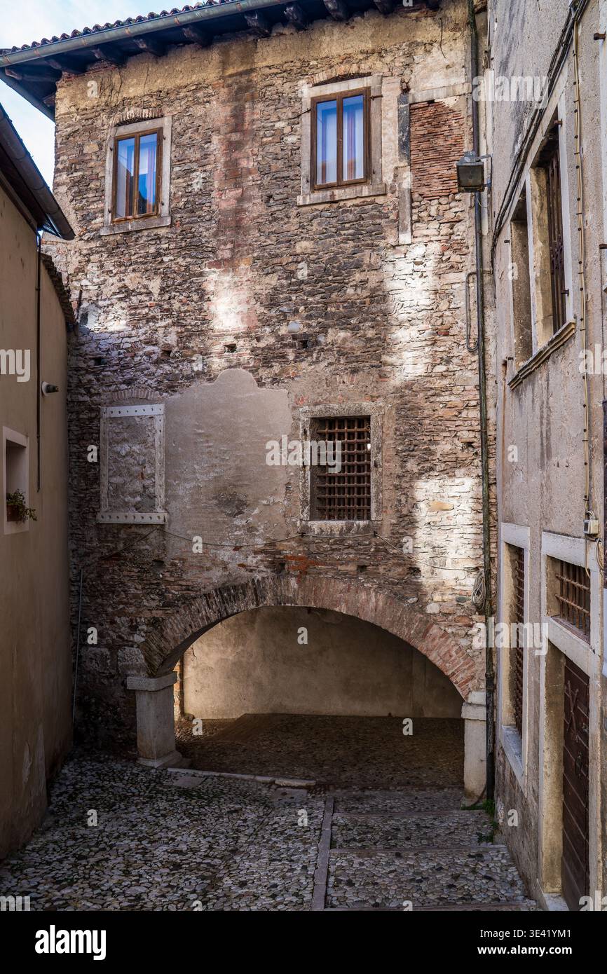 Vue évocatrice d'une ruelle historique à Feltre, Belluno. L'image montre un imposant bâtiment en pierre et brique avec une grande arche au-dessus de cobb traditionnel Banque D'Images