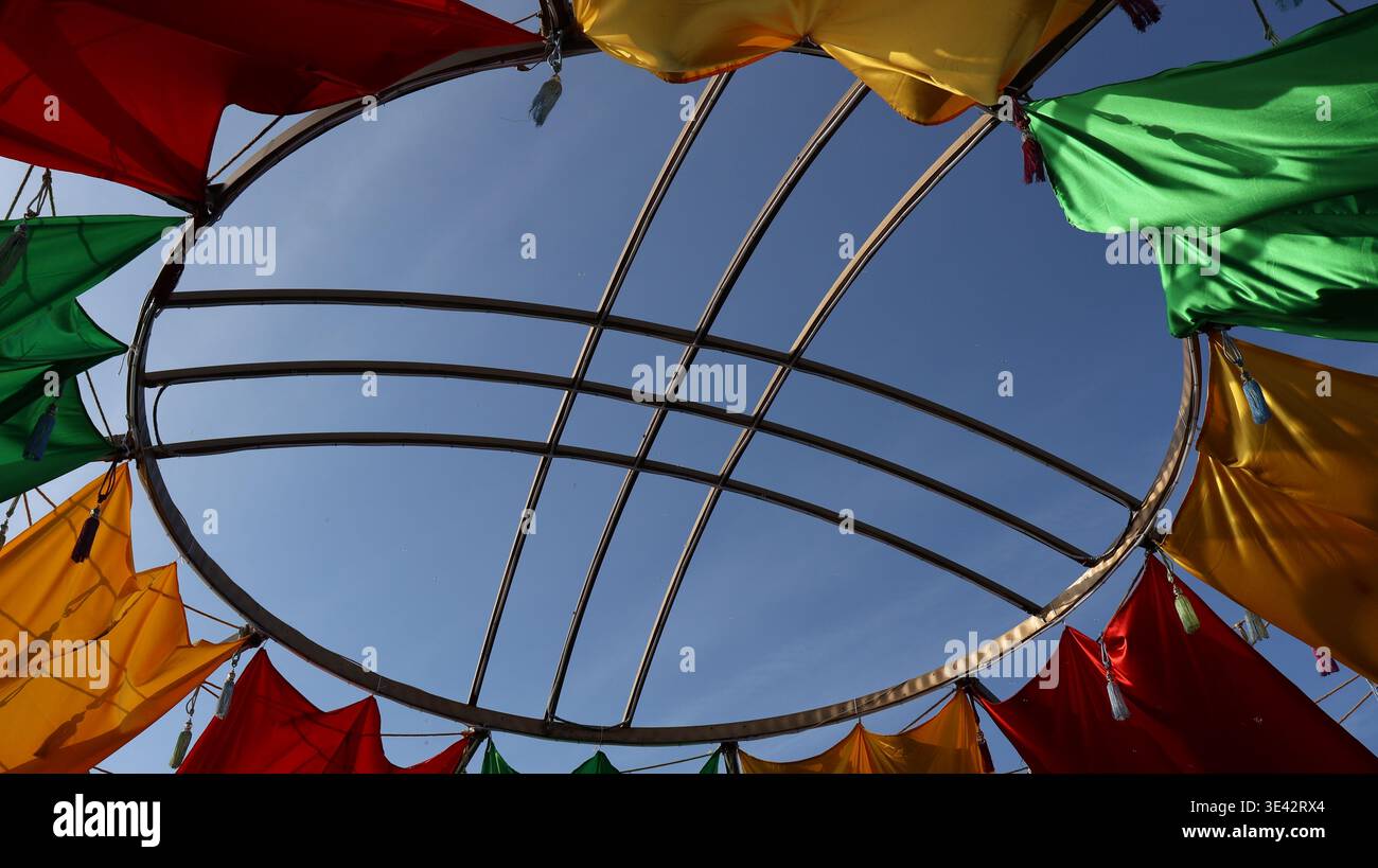 Vue vers le haut d'un cadre circulaire en métal décoré de panneaux de tissu colorés contre un ciel bleu clair. Composition abstraite vibrante avec stru géométrique Banque D'Images