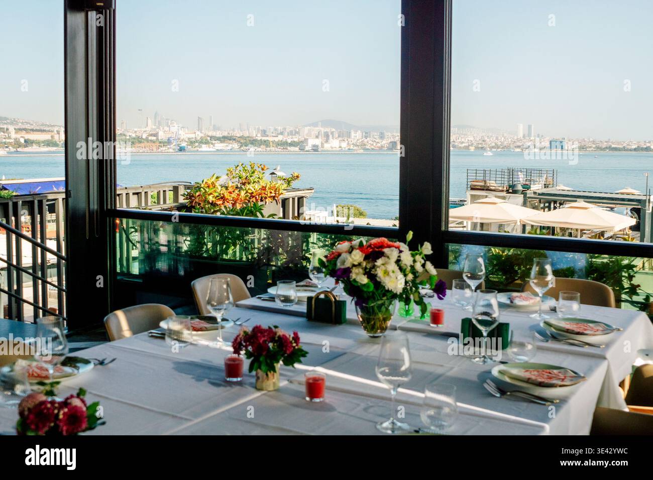 Waterfront Dinner Setup surplombant Port, draps blancs, bouquets de fleurs mixtes, chandelles votives, . Banque D'Images