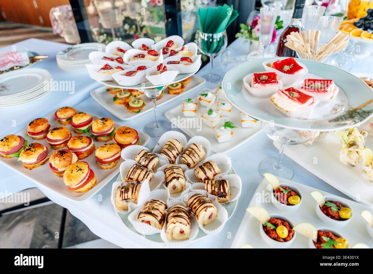 Canapés assortis et mini-pâtisseries sur plateaux blancs à la station de réception intérieure polie. Banque D'Images