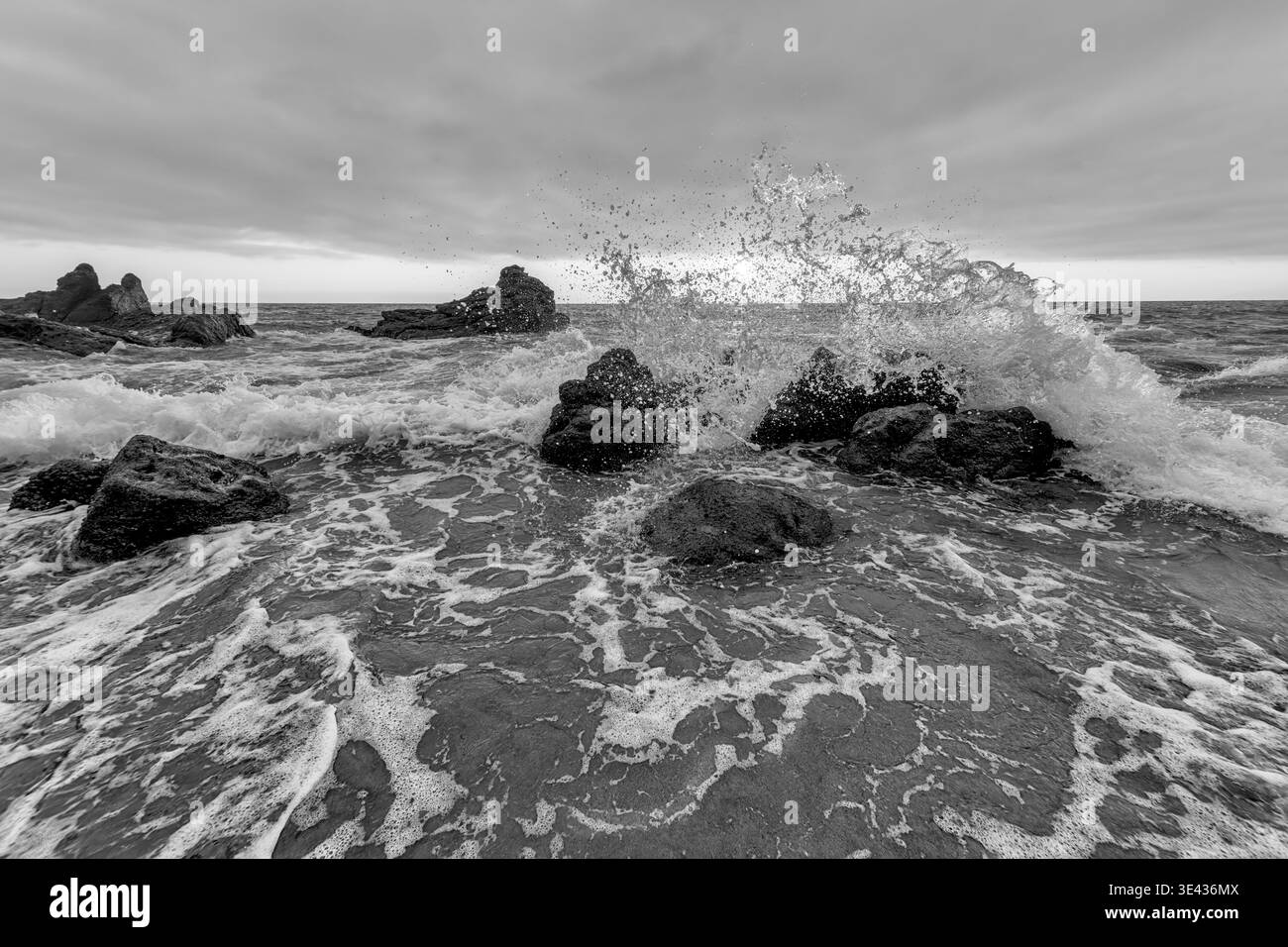 Une vague océanique se brise sur les rochers coupant contre Un brillant Sunset Horizon Noir et Blanc Banque D'Images