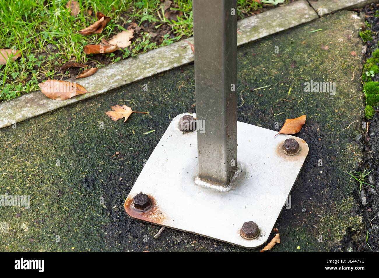 Gros plan de la plaque de base métallique fixée avec des boulons rouillés sur la chaussée. Concept de construction, durabilité, usure et infrastructure Banque D'Images