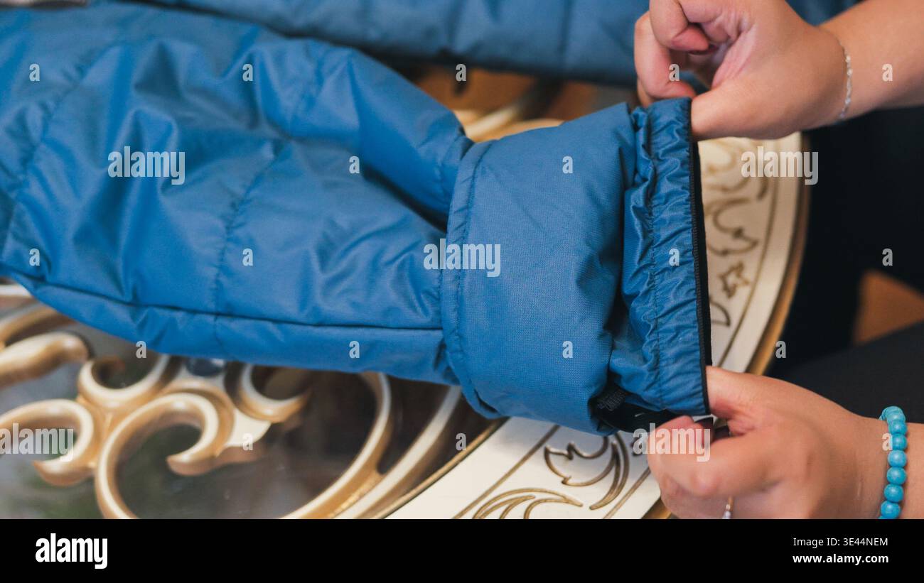 Personne ajustant le poignet élastique sur la veste en duvet bleu, se préparant pour le temps froid Banque D'Images