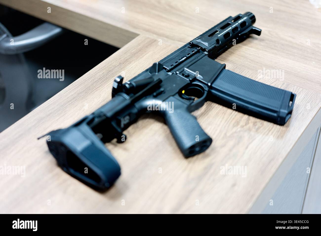 Fusil noir de style AR-15 avec chargeur amovible reposant sur un bureau en bois dans un cadre de bureau Banque D'Images