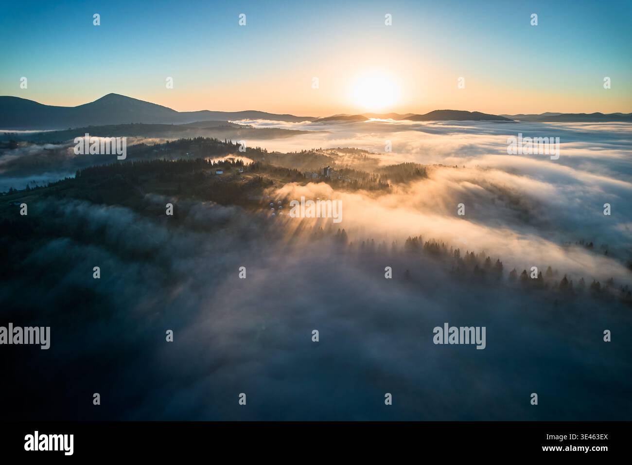 Superbe vue aérienne du lever du soleil sur le paysage montagneux, avec un brouillard épais couvrant les vallées et les collines. Les rayons dorés du soleil traversent la brume, projetant une lueur sereine sur toute la scène. Banque D'Images