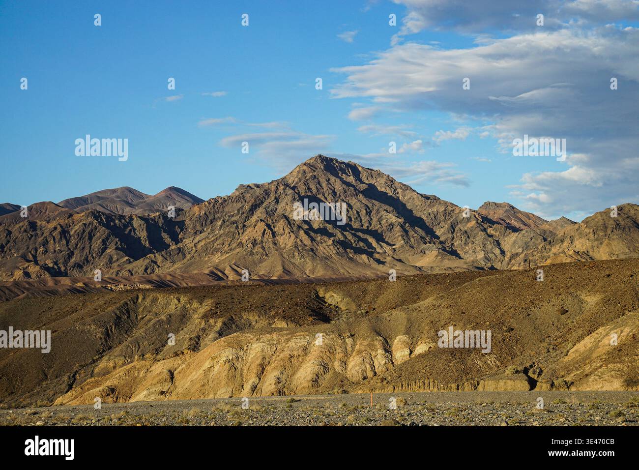 Montagnes désertiques rocheuses s'élevant au-dessus de collines arides sous le ciel bleu avec des nuages dispersés dans un paysage sauvage aride Banque D'Images