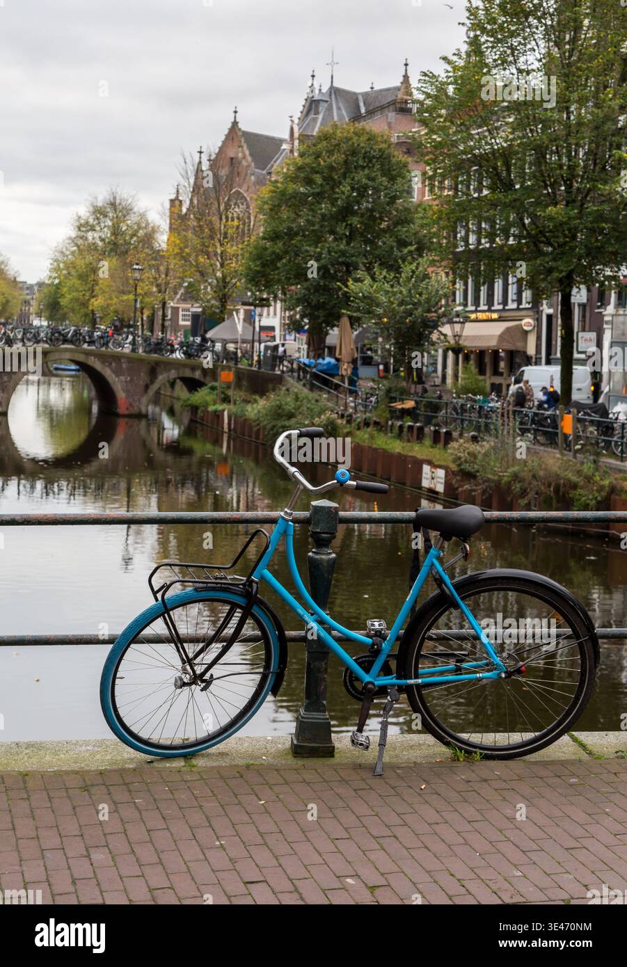 Un vélo bleu appuyé contre des balustrades métalliques sur un pont au-dessus de l'un des canaux d'Amsterdam, avec des arbres d'automne en arrière-plan Banque D'Images