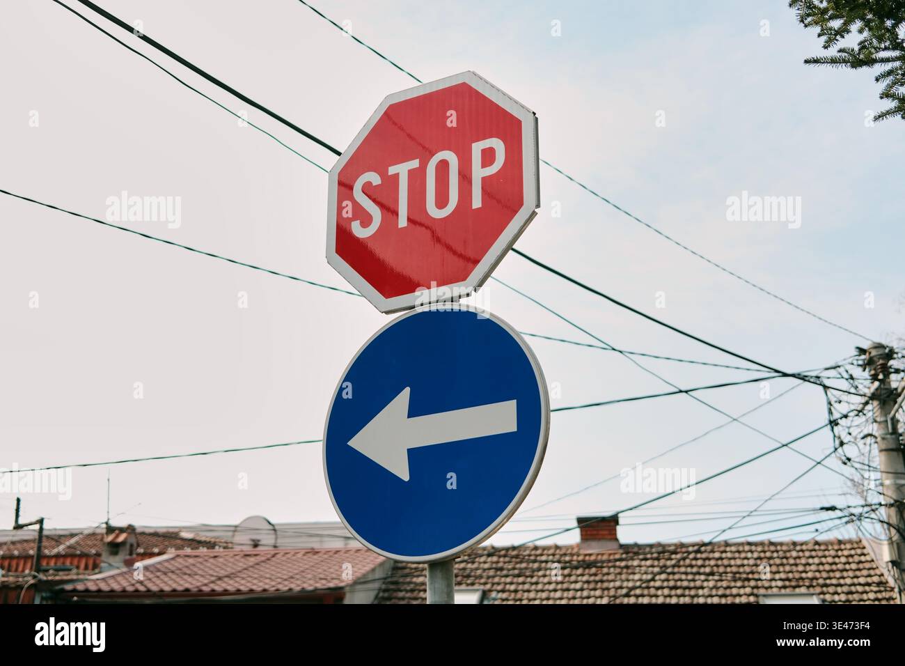 Panneau d'arrêt et panneau de flèche directionnelle sur la rue de la ville avec des fils et des maisons en arrière-plan. Idéal pour les règles de circulation, la navigation, les infrastructures urbaines et Banque D'Images